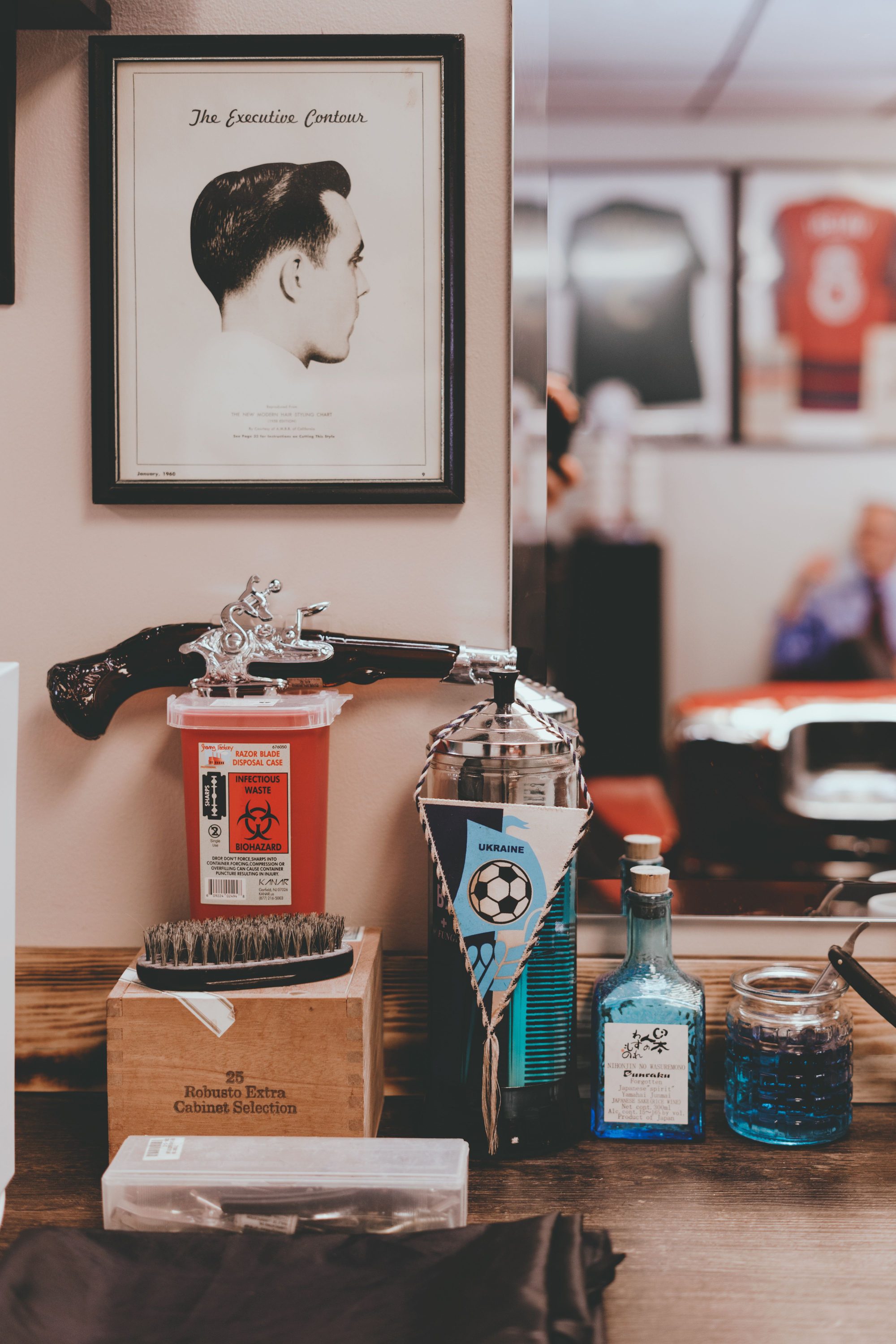 Close-up of a barbershop grooming station with a straight razor, shaving brush, apothecary bottles, and a vintage "Executive Contour" haircut chart on the wall